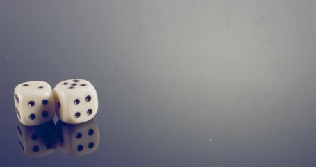 Slow motion macro shot of white dice falling and rolling on reflective surface