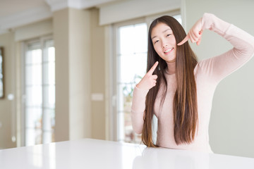 Obraz na płótnie Canvas Beautiful Asian woman wearing casual sweater on white table smiling confident showing and pointing with fingers teeth and mouth. Health concept.