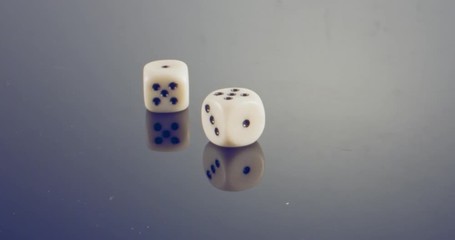 Slow motion macro shot of white dice falling and rolling on reflective surface