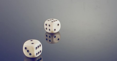 Slow motion macro shot of white dice falling and rolling on reflective surface
