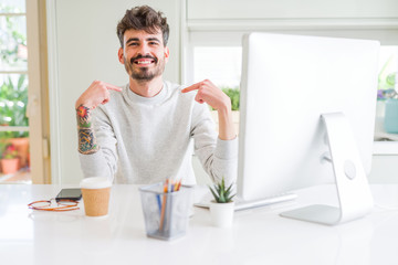 Young man working using computer looking confident with smile on face, pointing oneself with...