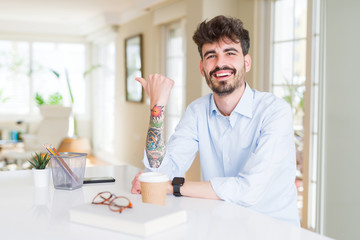 Young business man working smiling with happy face looking and pointing to the side with thumb up.