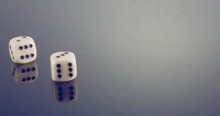 Slow motion macro shot of white dice falling and rolling on reflective surface