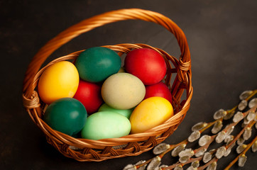 Easter eggs in a basket and willow branches on a stone background