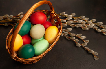 Easter eggs in a basket and willow branches on a stone background