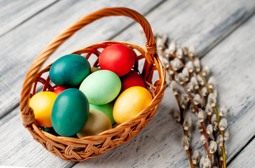 Easter eggs in a basket and willow branches on a wooden background