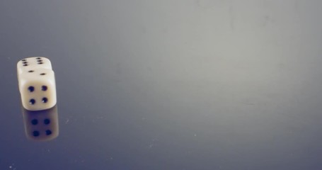 Slow motion macro shot of white dice falling and rolling on reflective surface