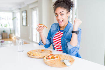 Young african american woman eating two homemade cheese pizzas screaming proud and celebrating victory and success very excited, cheering emotion