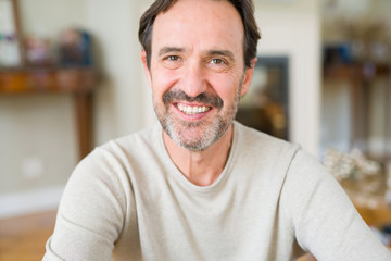 Handsome middle age man sitting on the floor smiling at the camera at home