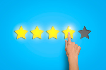 Female hand leaves a rating of four stars out of five possible on a blue background. Concept of evaluating something