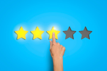 Female hand leaves a rating of three stars out of five possible on a blue background. Concept of evaluating something