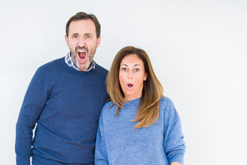 Beautiful middle age couple in love over isolated background In shock face, looking skeptical and sarcastic, surprised with open mouth