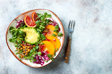 Vegan, detox Buddha bowl with turmeric roasted  chickpeas, greens, avocado, persimmon, blood orange, nuts and pomegranate. Top view, flat lay, copy space