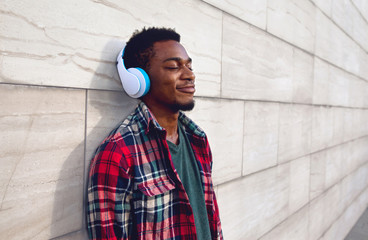 Fototapeta na wymiar Portrait happy smiling african man in wireless headphones enjoying listening to music on city street over gray wall background