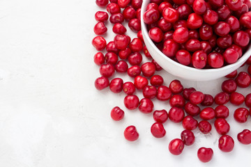 Fresh cherries in a white plate and scattered around on a light stone background