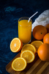A glass of Fresh Orange Juice with a Tube, Orange slices, Oranges, white Cloth on a Dark Blue Background