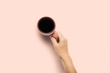 A hand is holding a cup with hot coffee on a pink background. Breakfast concept with coffee or tea. Good morning, night, insomnia. Flat lay, top view