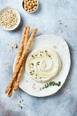 Homemade hummus with thyme, olive oil and pine nuts with grissini bread sticks. Middle Eastern traditional and authentic arab cuisine. Top view, flat lay, overhead