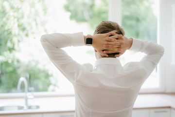 Businessman looking out of the kitchen window of his new home, hands behind head