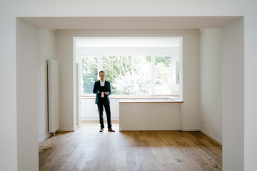 Estate agent waiting in newly refurbished home, holding laptop