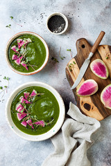 Homemade green spring spinach cream soup decorated with watermelon radish, black sesame seeds and microgreens