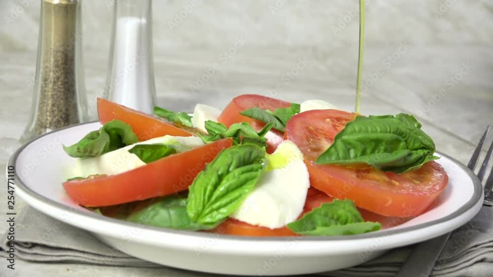 Poster pouring olive oil on a caprese salad, slow motion