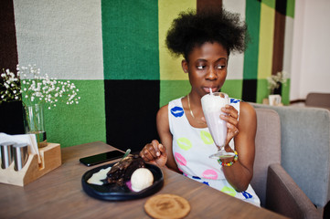 Сheerful african american young woman in summer dress at cafe drinking milkshake.