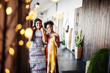 Fototapeta premium Two black african girlfriends at summer dresses posed in cafe at mirror.
