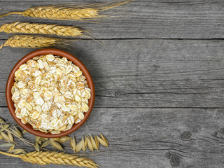Cereal flakes in brown plate on table out of grey boards. Spikelets of different types of grain.