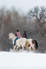 two girls riding horses bareback in winter on a snow covered field