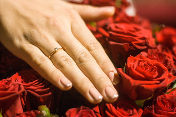 Bride hand a with wedding ring and red roses as background