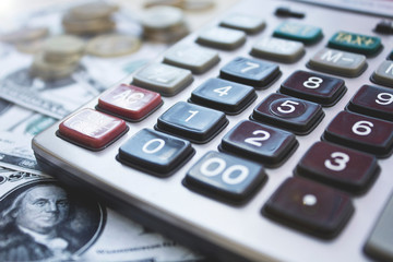 Calculator with dollars and coins on wooden background.