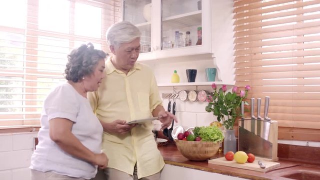 Asian elderly couple using tablet prepare ingredient for making food in the kitchen, Couple use organic vegetable for healthy food at home. Lifestyle senior family making food at home concept.