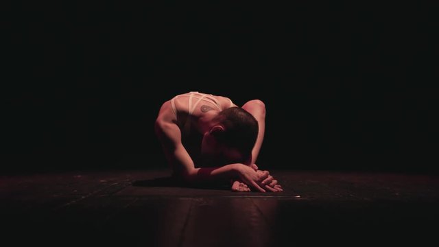 Female gymnast stretching on dark stage