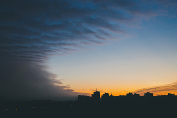 Cityscape with wonderful varicolored vivid dawn. Amazing dramatic blue cloud sky above dark...
