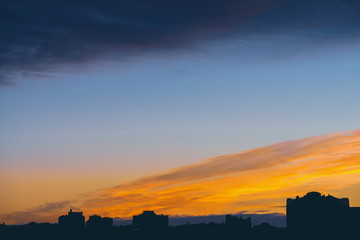 Cityscape with wonderful varicolored vivid dawn. Amazing dramatic blue cloud sky above dark...