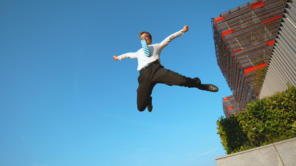 LOW ANGLE: Happy businessman jumps off a concrete ledge with outstretched arms