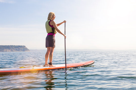 Happy, healthy woman wearing a life jacket paddleboarding. Women's outdoor adventure summer water sports.