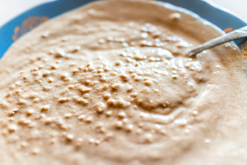 Macro closeup of brown roasted or raw oat or buckwheat groat grain breakfast Ukrainian or Russian food porridge cooked raw in blender with spoon in bowl