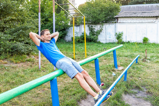 Fit man doing calisthenics workout crunches sit ups on parallel horizontal bars exercise in outdoor park in Rivne, Ukraine playground