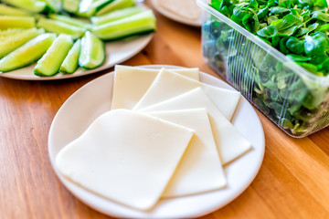 Wooden table setting of healthy vegan vegetarian lunch green vegetables and cheese slices with salad cucumbers in home