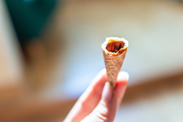 Woman hand holding one white vanilla ice cream gelato cone almost eaten bottom with background on...
