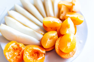 Closeup of cut fruit pear or apple slices and apricot plum halves on white plate macro and orange yellow vibrant color snack