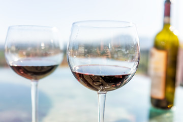 Terrace patio in Italy with bottle and two glasses macro of red wine on glass table with bokeh background of mountains