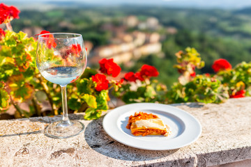 Closeup of vegetarian vegan lasagna slice on plate and white wine on balcony terrace by red...