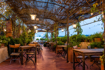Typical Italian rooftop restaurant wooden tables in Tuscany with covered roof pergola vine canopy with empty seats, chairs and nobody in rustic romantic architecture