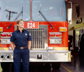 Smiling female woman firefighter in uniform with fire engine truck at station. Happy, confident, successful public service career professional.
