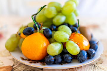 Naklejka na ściany i meble Closeup of whole mandarin satsuma orange and green grapes fruits with blue red grapes pile heap on plate bowl in winter autumn season