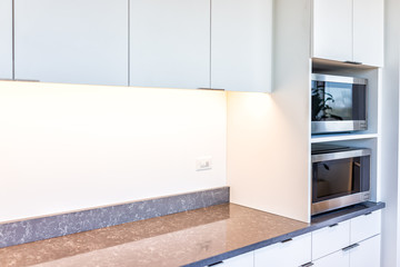 Modern white minimalist kitchen features cabinets with granite countertop and microwave toaster...