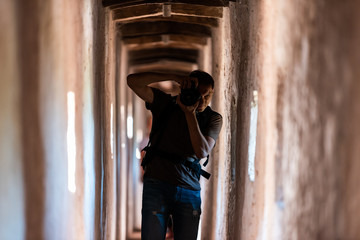 Young man silhouette taking picture in light standing in fortress tunnel passage in Italy during summer with walls by windows in Castiglione del Lago